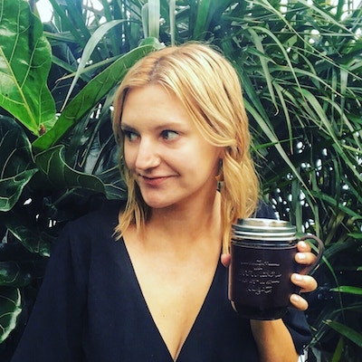 A woman holding a mason jar in front of a plant.