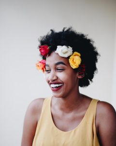 A black woman wearing a flower crown and smiling, her skin glowing from the best moisturizers.