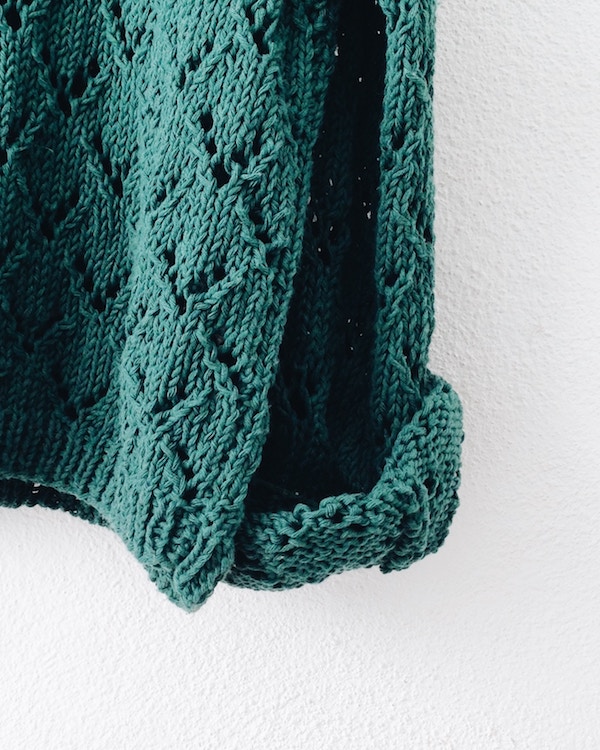A green knitted sweater, bought as second-hand clothes, hanging on a wall.