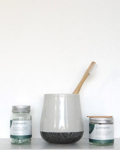 Two jars of zero waste toothpaste and a toothbrush on a shelf.