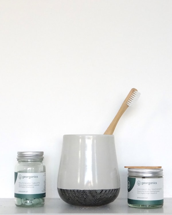 Two jars of zero waste toothpaste and a toothbrush on a shelf.