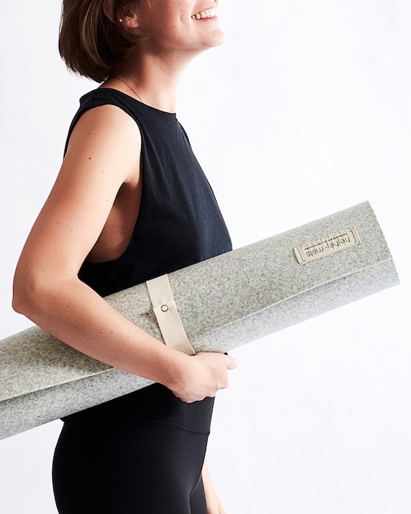 A woman holding an eco-friendly yoga mat in front of a white background.