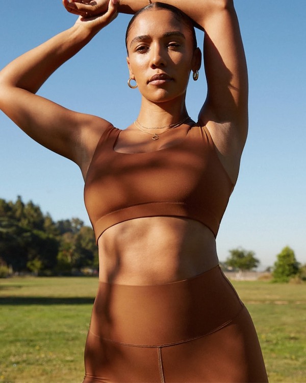 A woman in a brown sustainable activewear sports bra posing in a field.