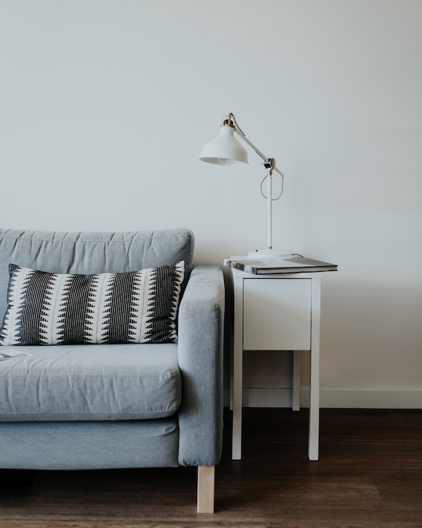A gray couch in a minimalist living room with a lamp.