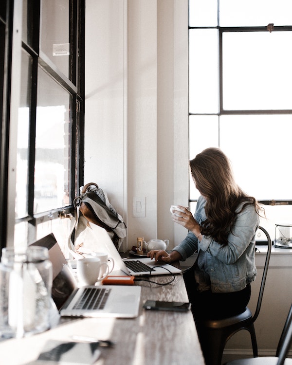 A woman sitting at a desk with a laptop and an eco-friendly cup of coffee.