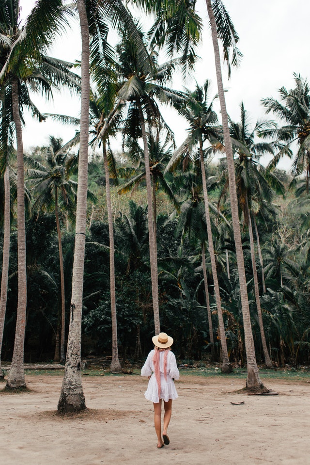 A woman walking through the sand with palm trees in the background, embodying sustainable travel.