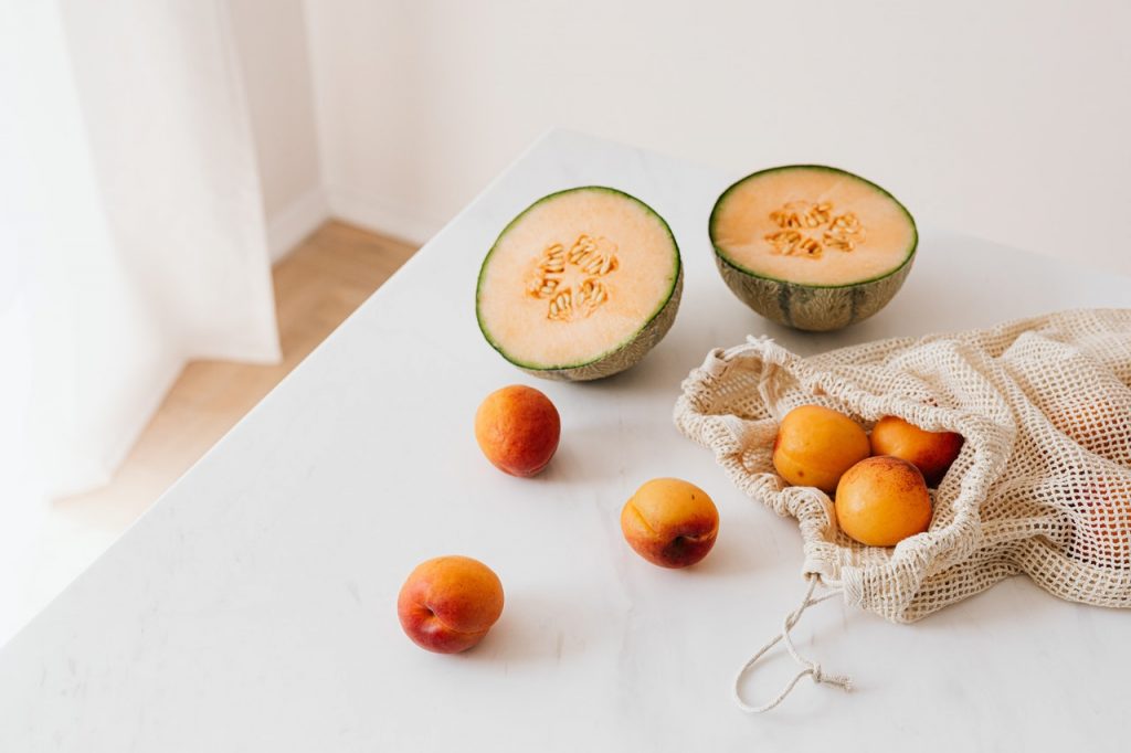 Melon and apricots in a Zero Waste bag on a white table.