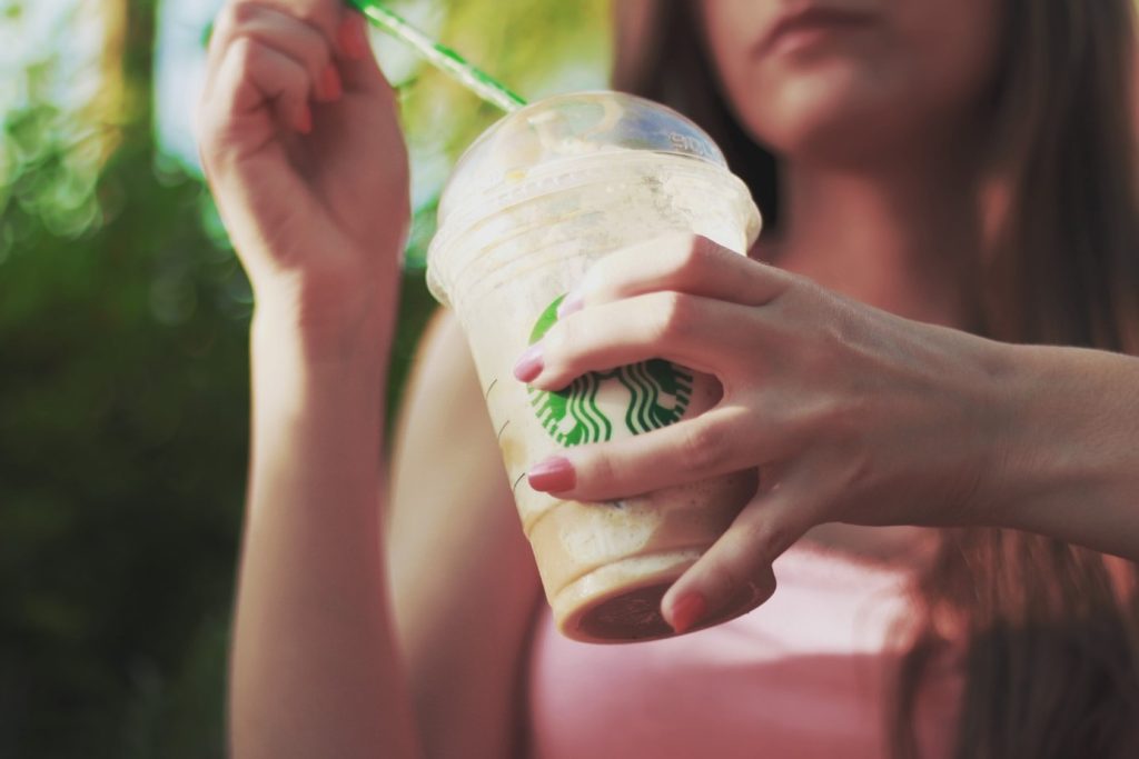 A woman is holding a Starbucks drink, unaware of its contribution to plastic pollution.